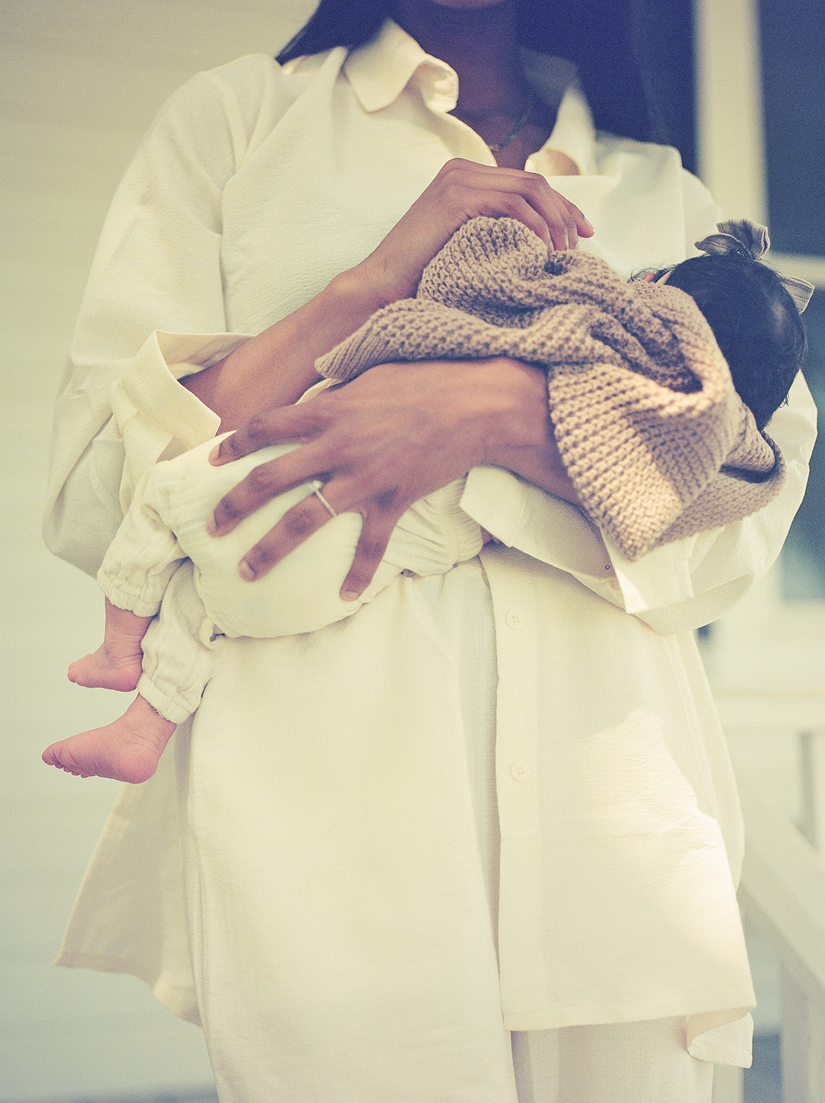 A mother holds a baby in a tan knit blanket
