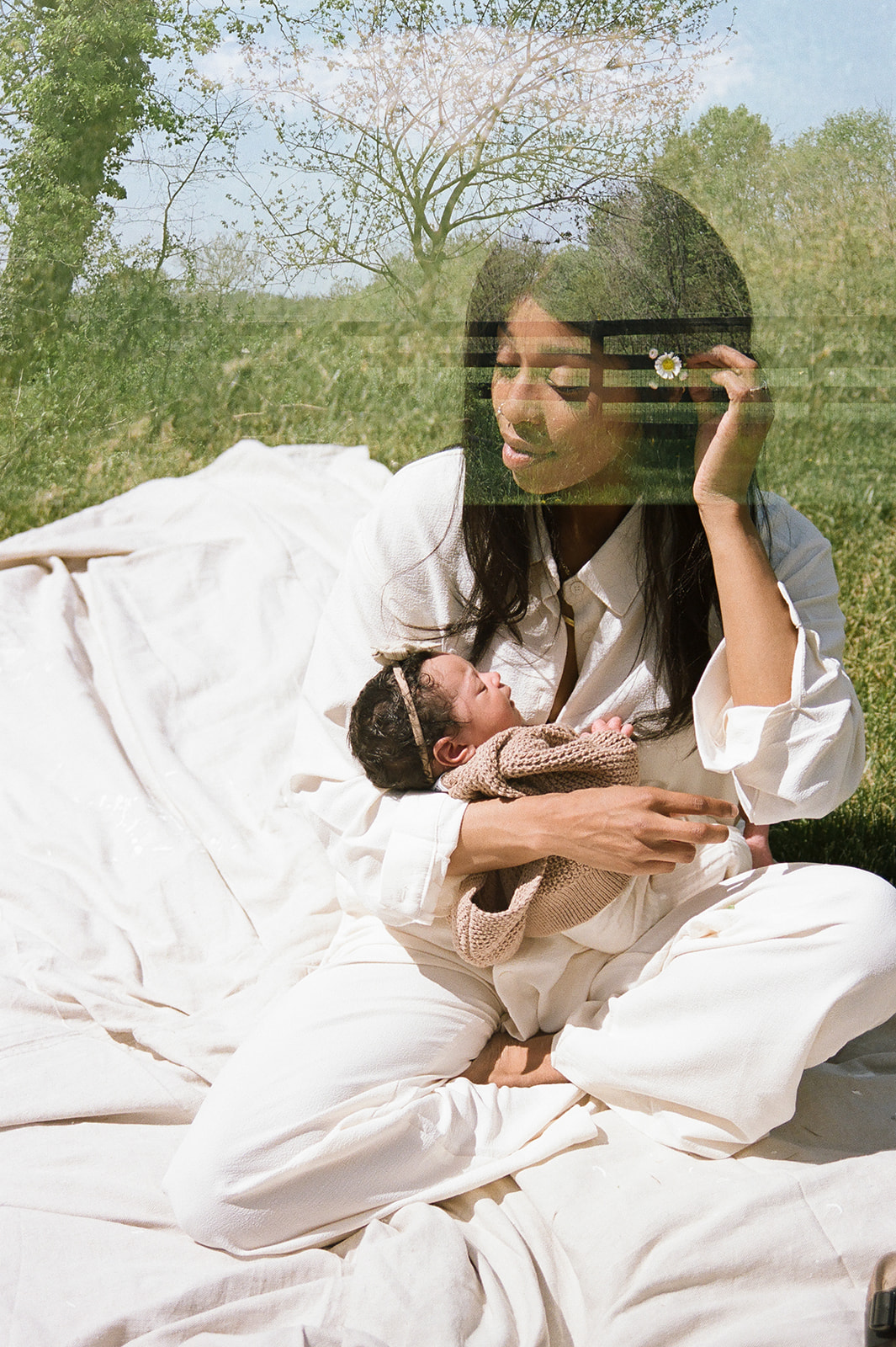 A film photp of a mother with a flowerbehind her ear holding a small baby 