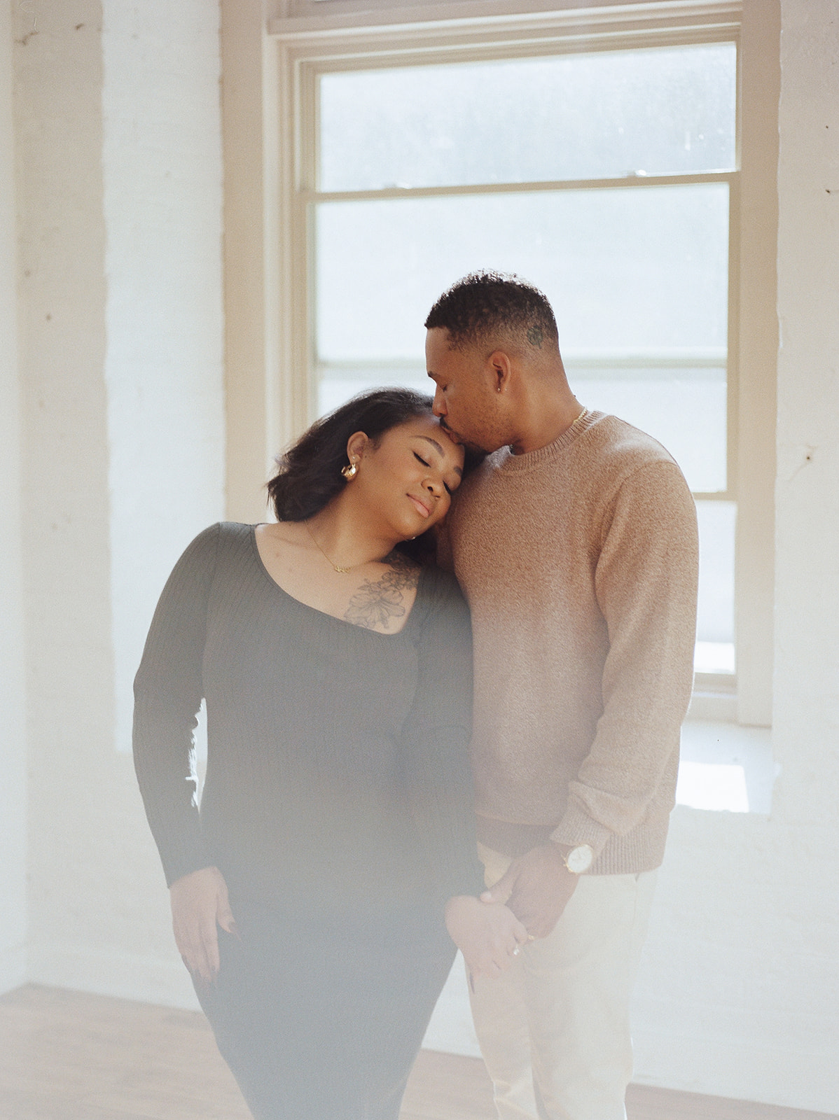 A man and wife embrace in a naturally lit space of a Baltimore photography studio