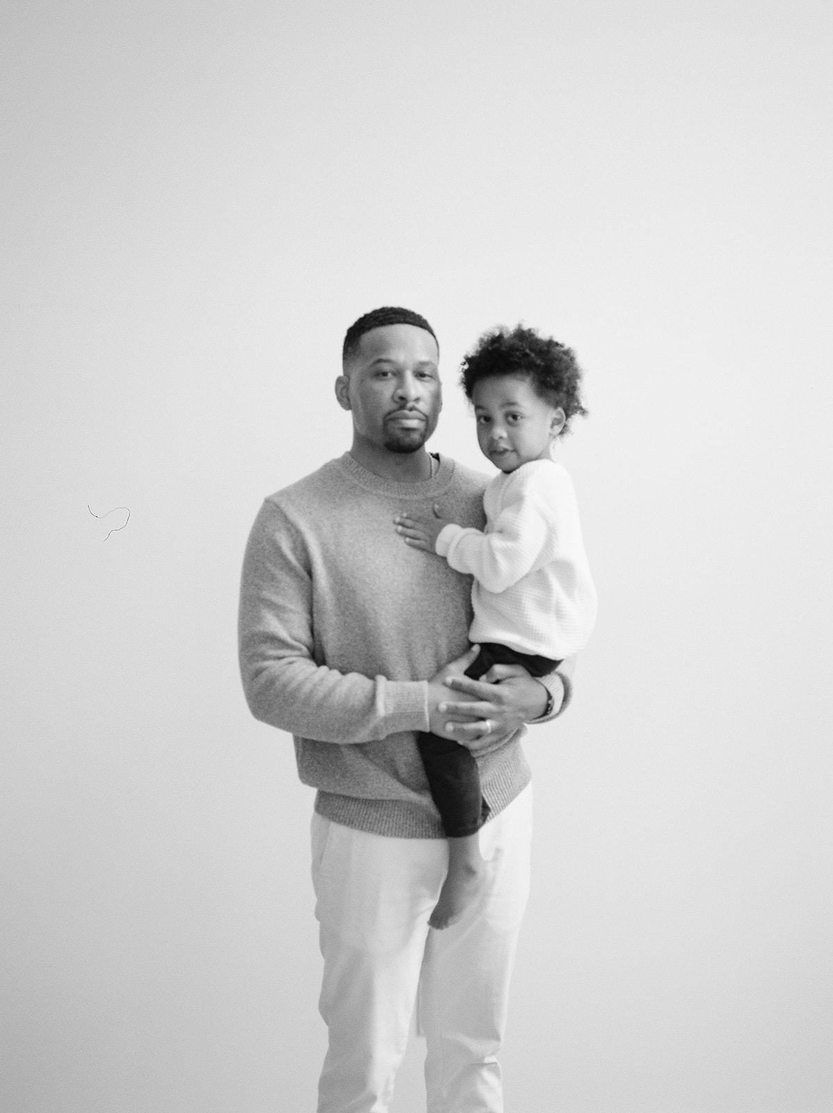 A father holds his toddler and stands against a blank backdrop