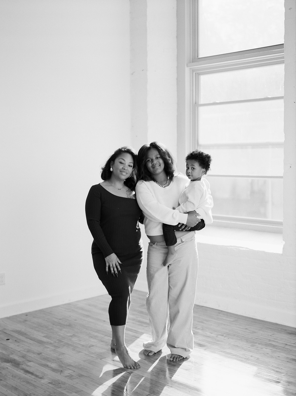 A mother, her teenage daughter, and toddler pose for family photos in front of a large window