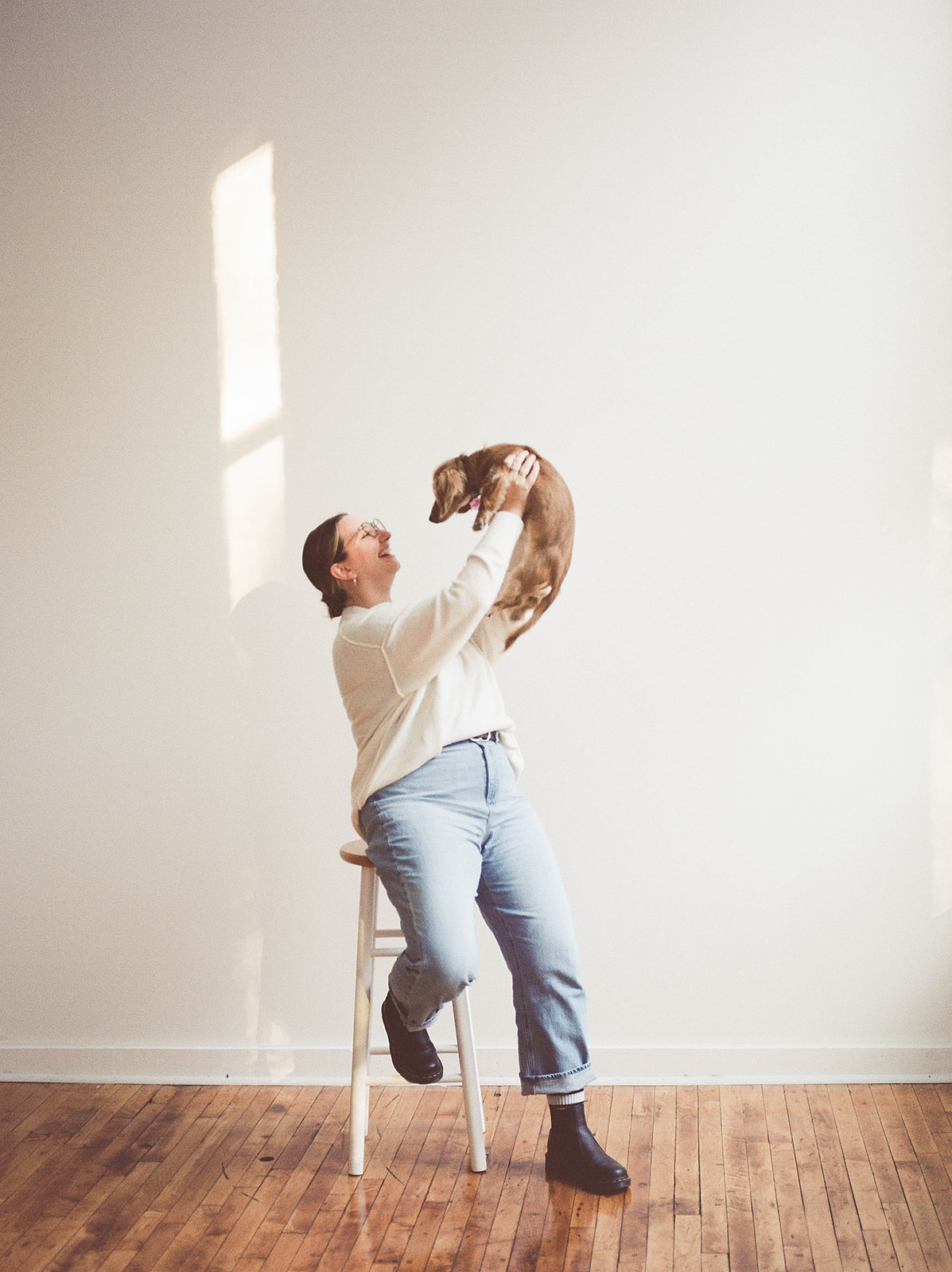A woman sits on a stool, holding a dachshund