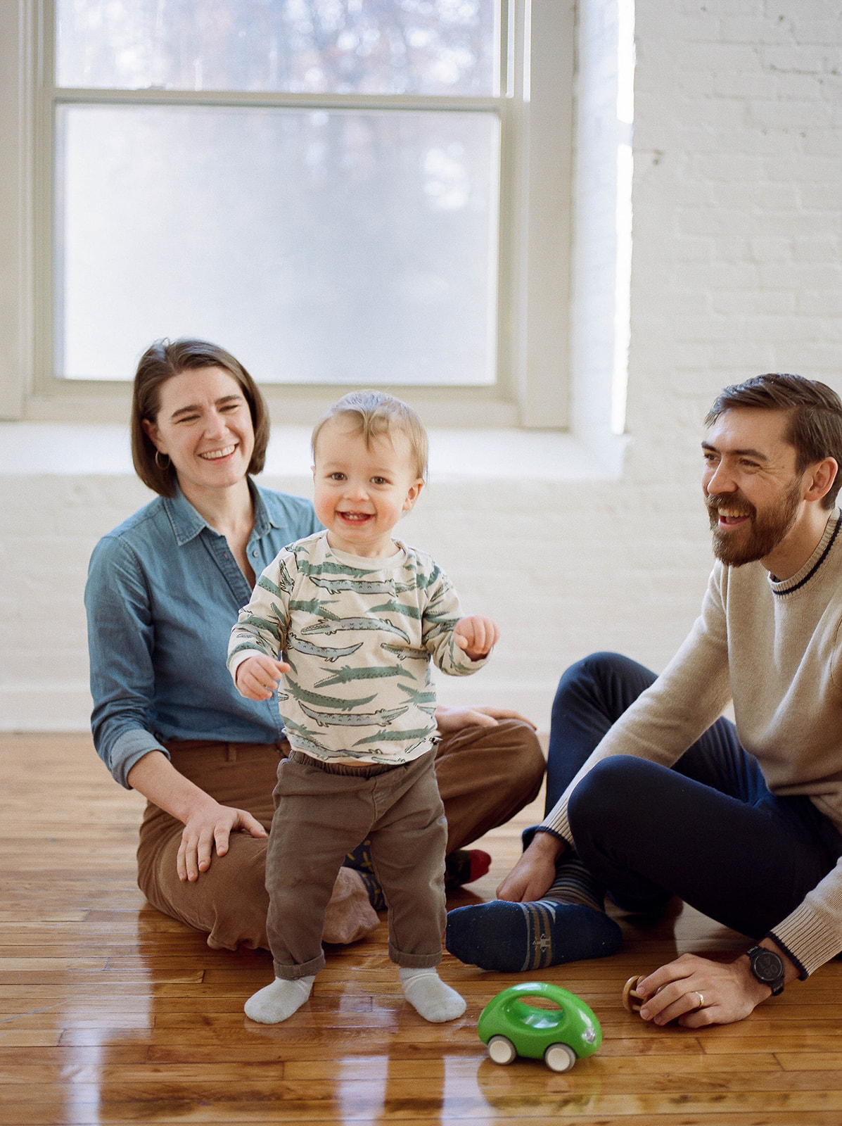 A husband and wife sit on the floor with their toddler