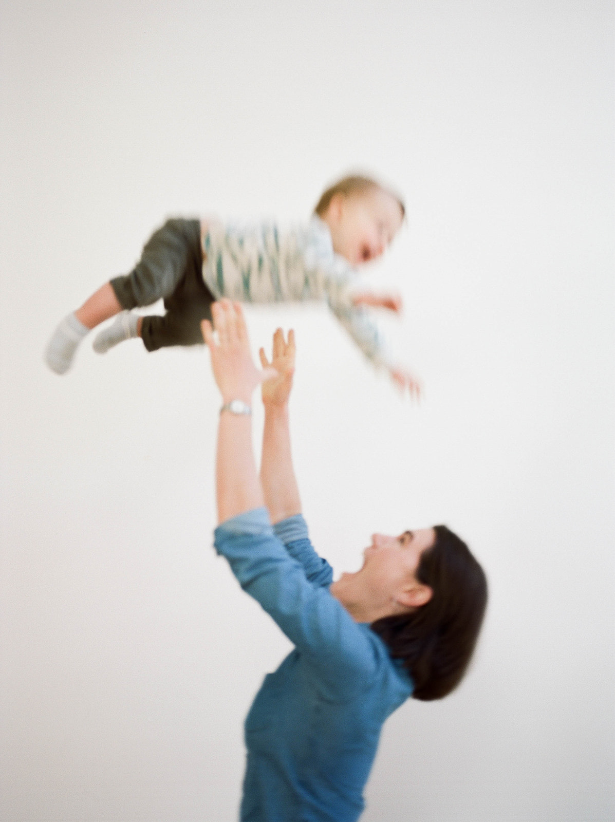 A mother tosses her toddler in the air during studio family photos