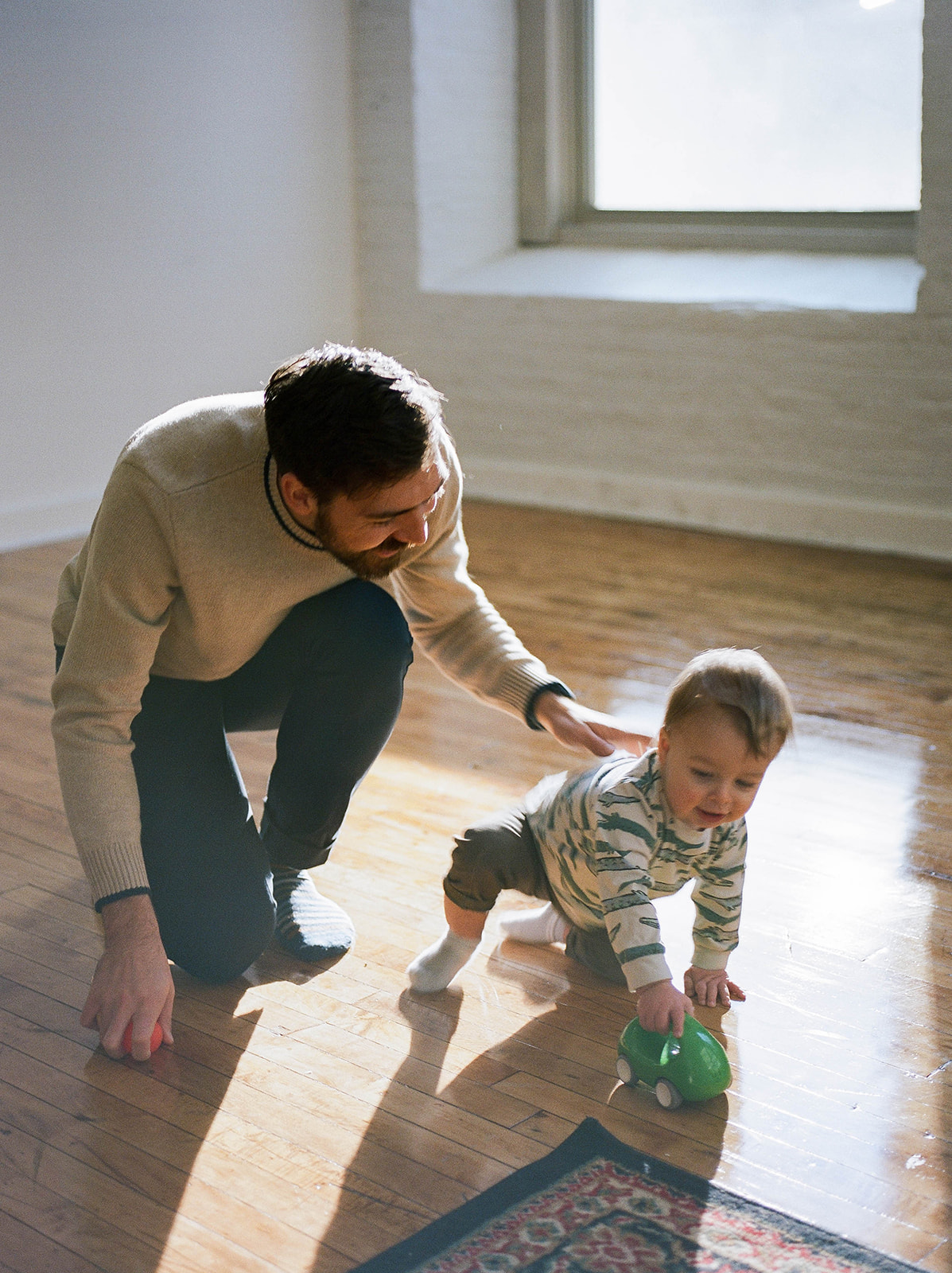 A dad sits on the floor playing with his toddler son during studio family photos in Baltimore