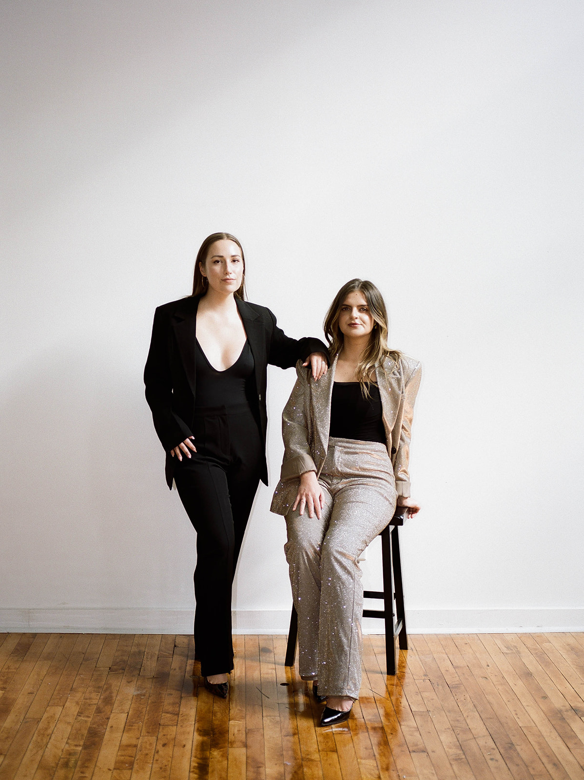 Two women, one sitting on a black stool, posing for their brand photos