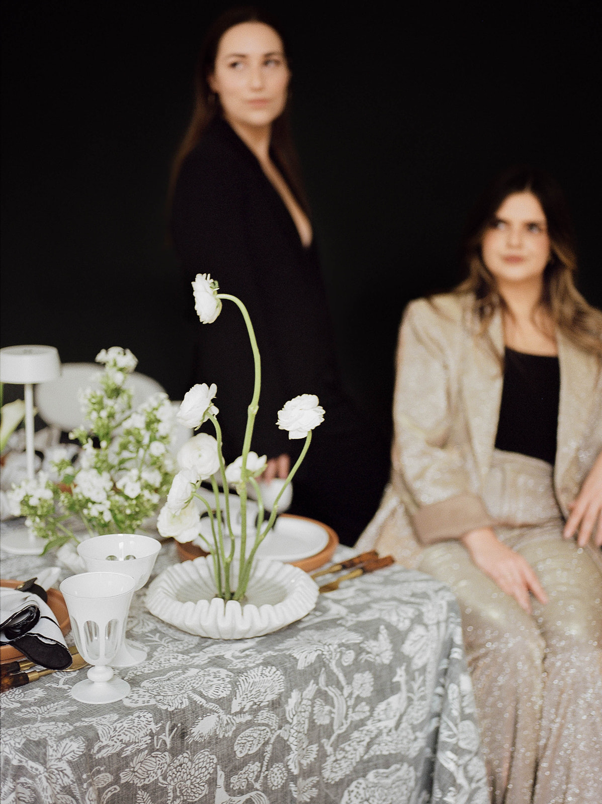 Brand photos of two wedding planners sitting at a table with abstract florals and a printed tablecloth