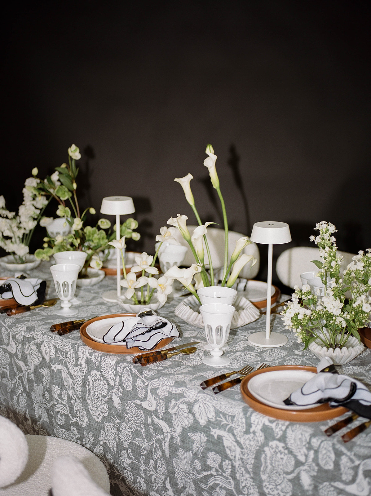 A film photo of a styled table with lilies, glasses, linen napkins, and small white lamps