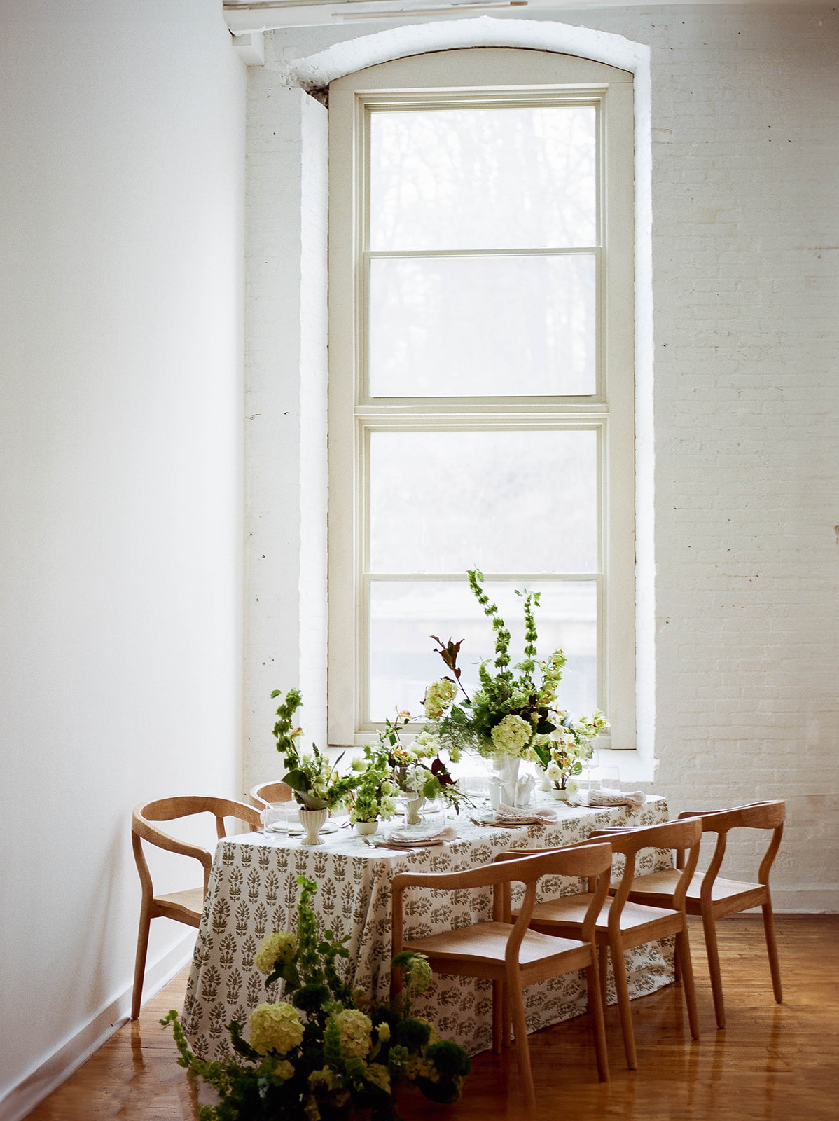 A table-scape with large abstract floral arrangements in front of a window