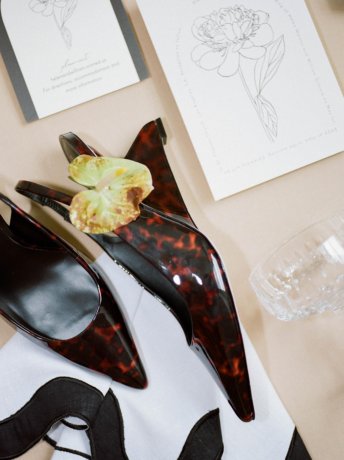 A flat lay with shoes, a crystal champagne glass, and wedding invitations