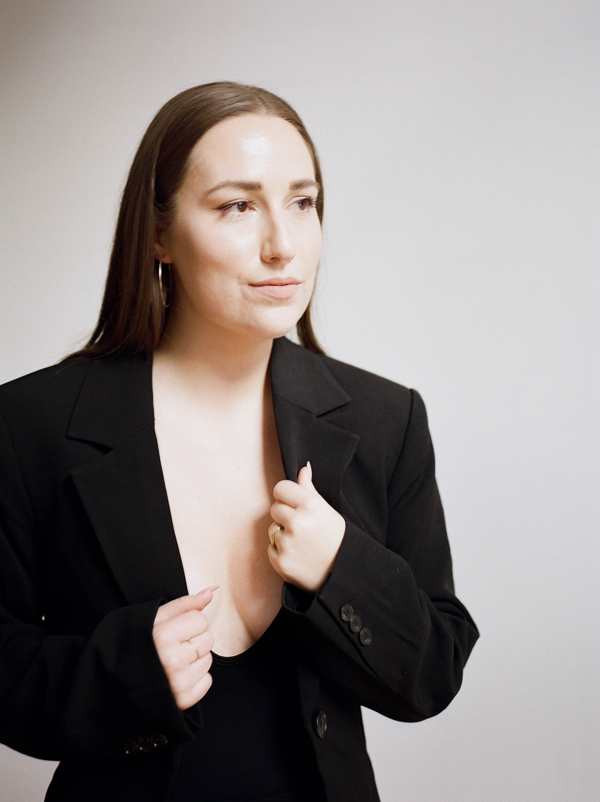 A woman with long brown hair and a black suit with a low cut V neck top