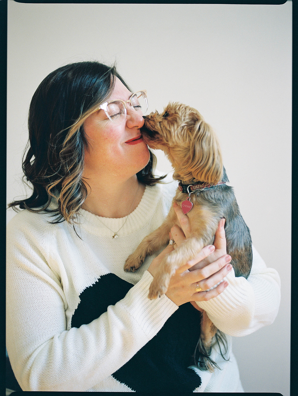 A small dog kisses a woman's face while she holds him