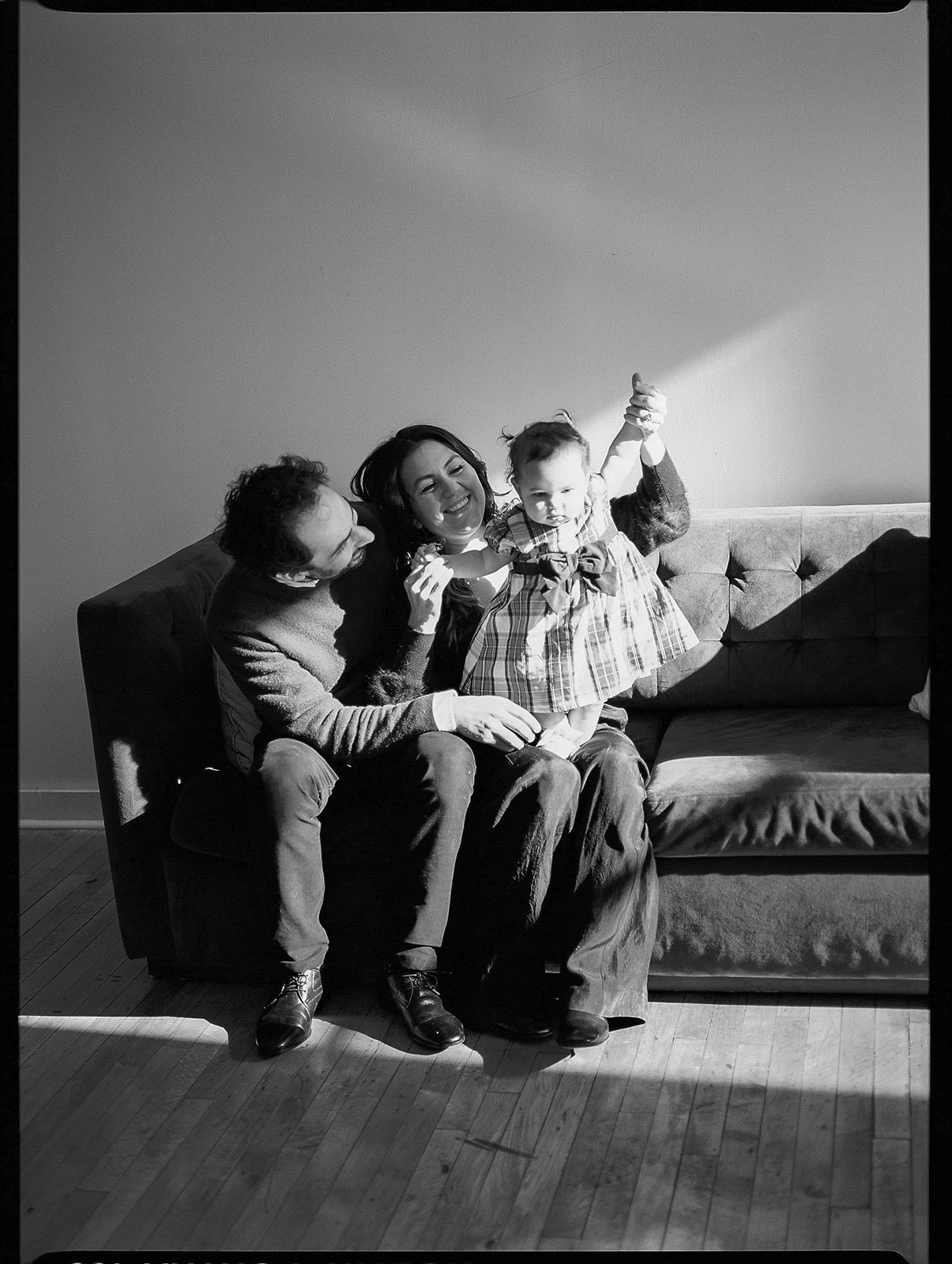 A black and white film photo of a man, woman, and baby on a grey couch