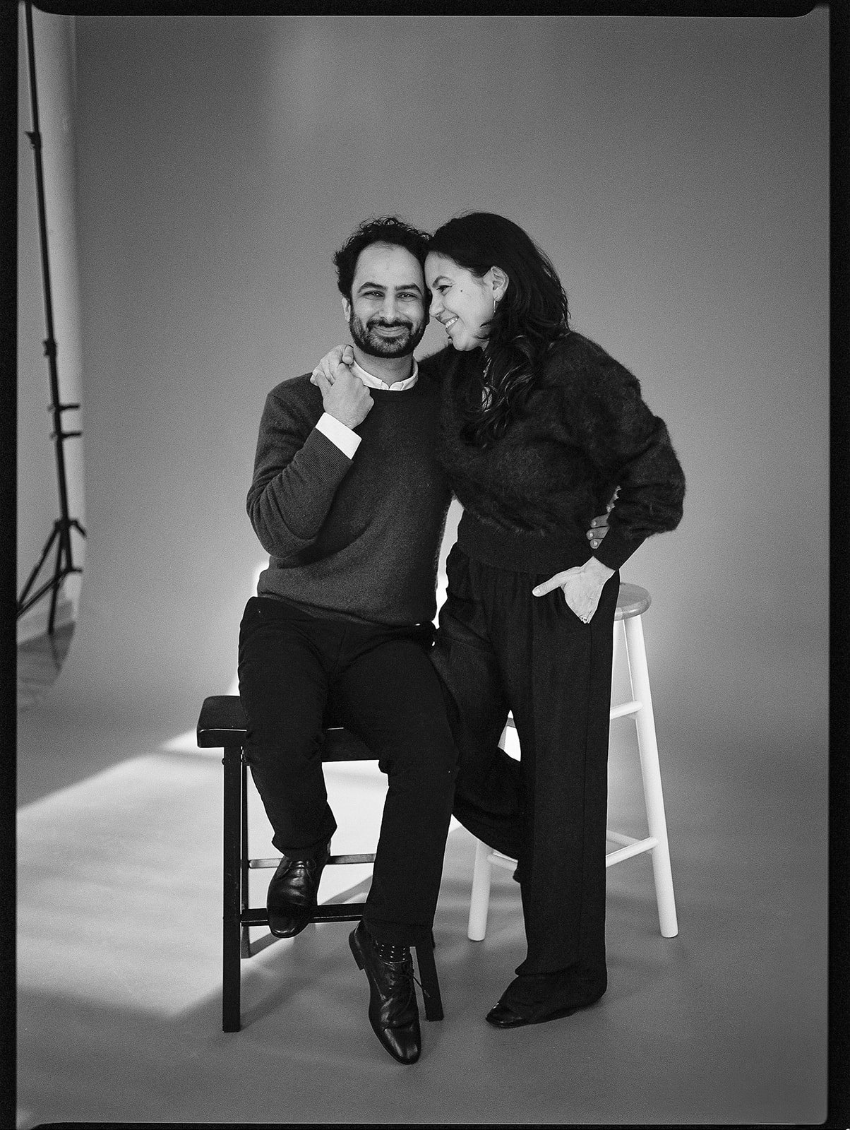 A black and white film photo of a husband and wife in front of a plain backdrop