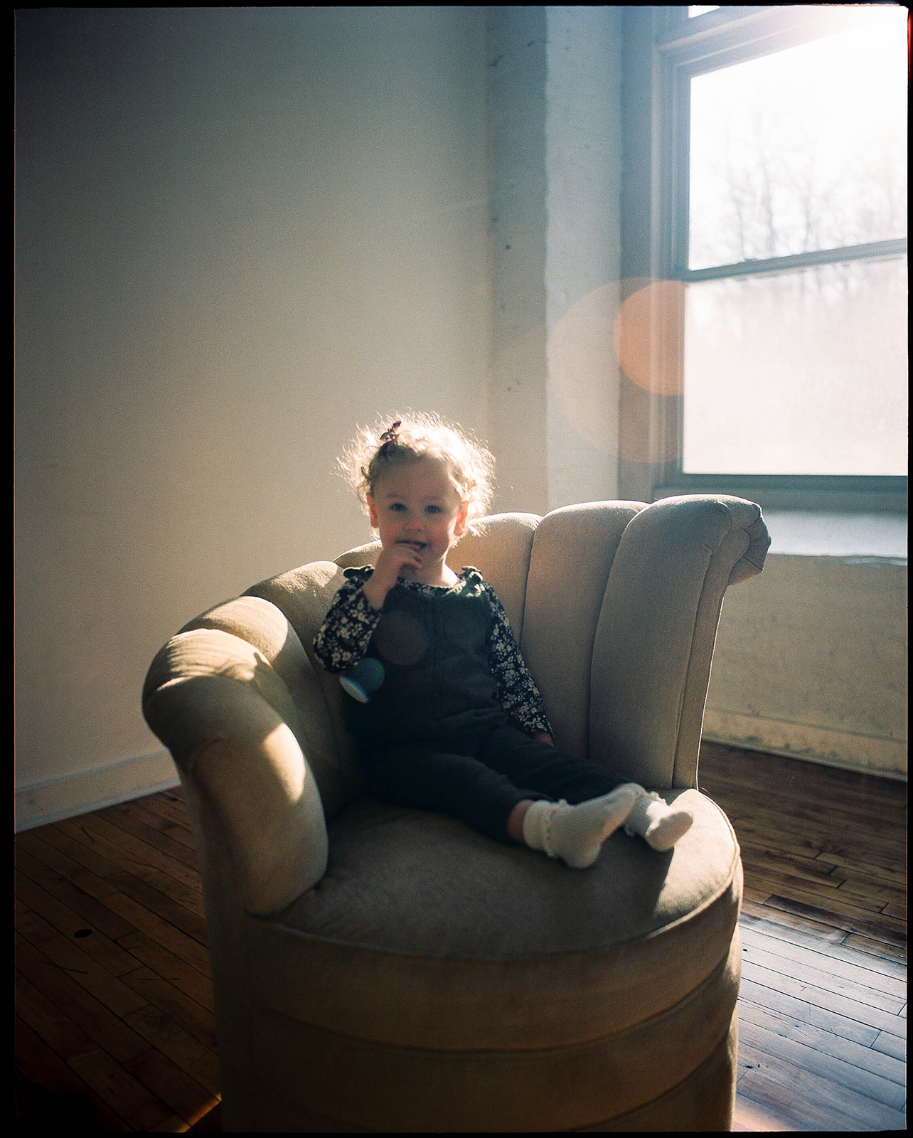 A little girl with short blonde curls sits in a large comfy chair