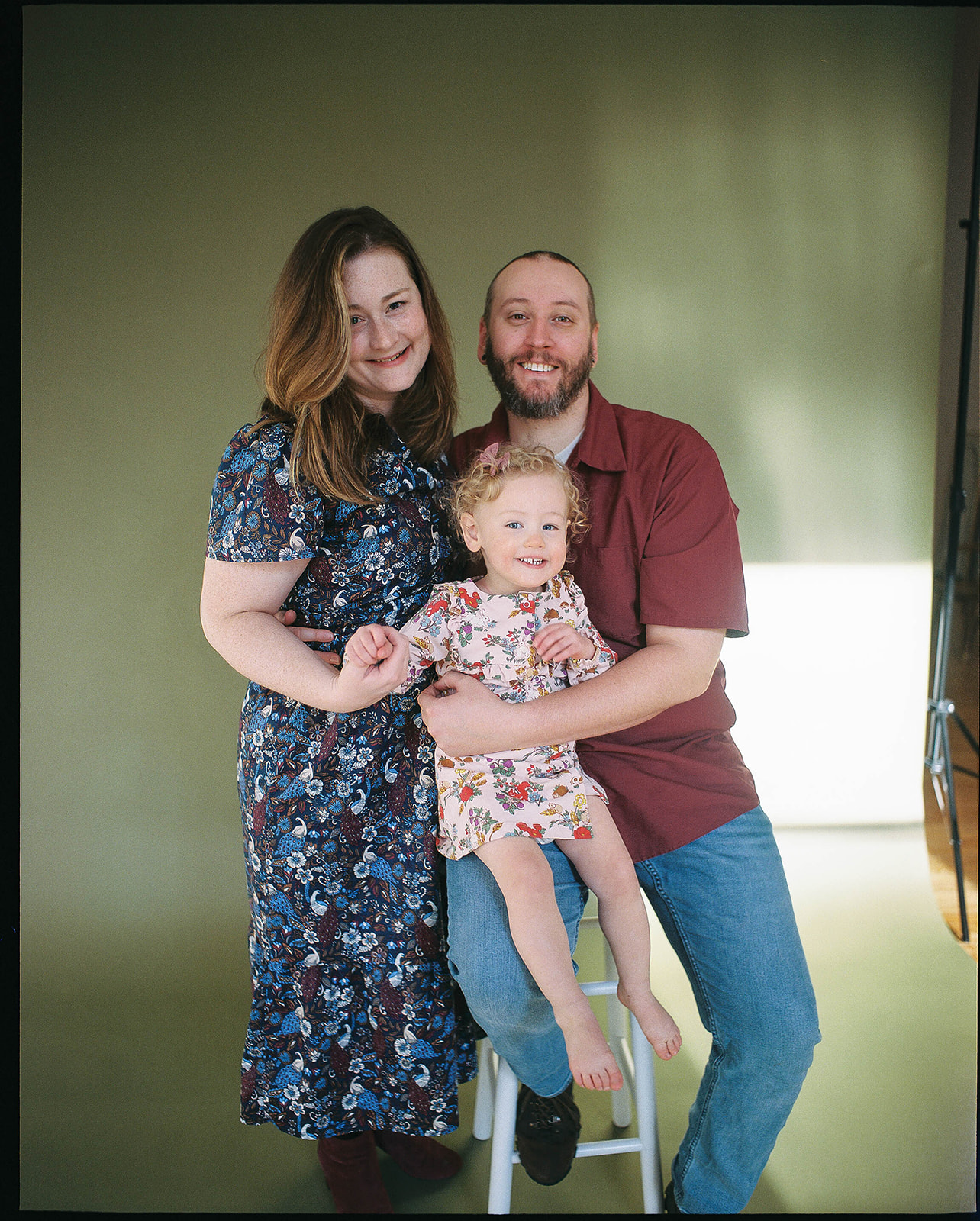 Family photos of a mother, father, and daughter in a Baltimore studio with white brick walls and natural hardwood floors