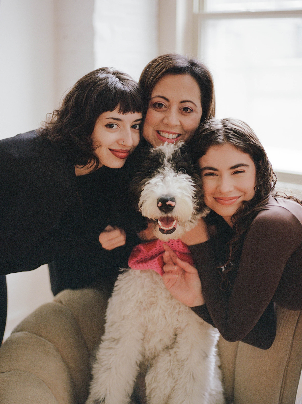 Three women cuddle with a black and white dog with curly fur