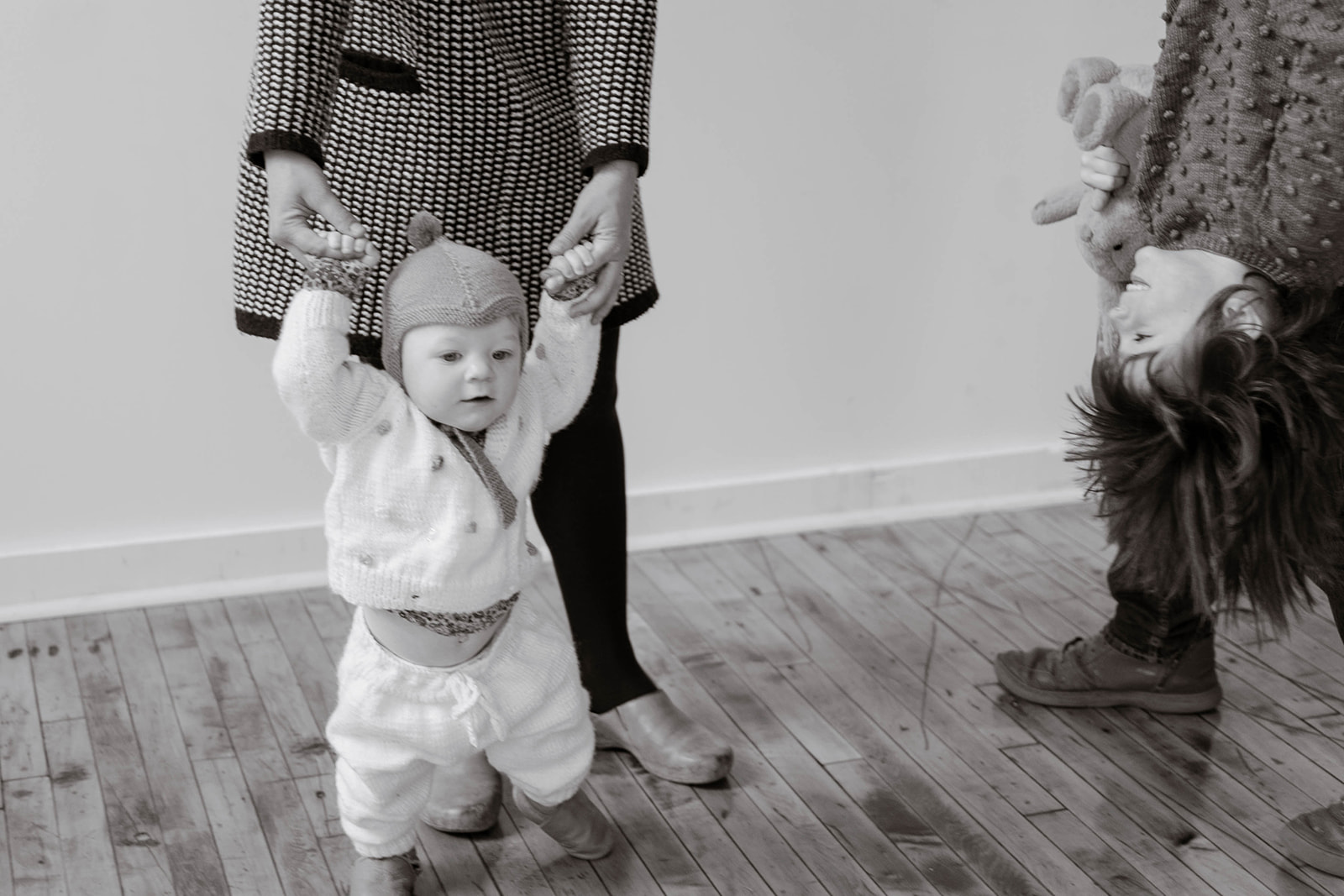 A mother holds her baby's hands while the baby takes tentative steps
