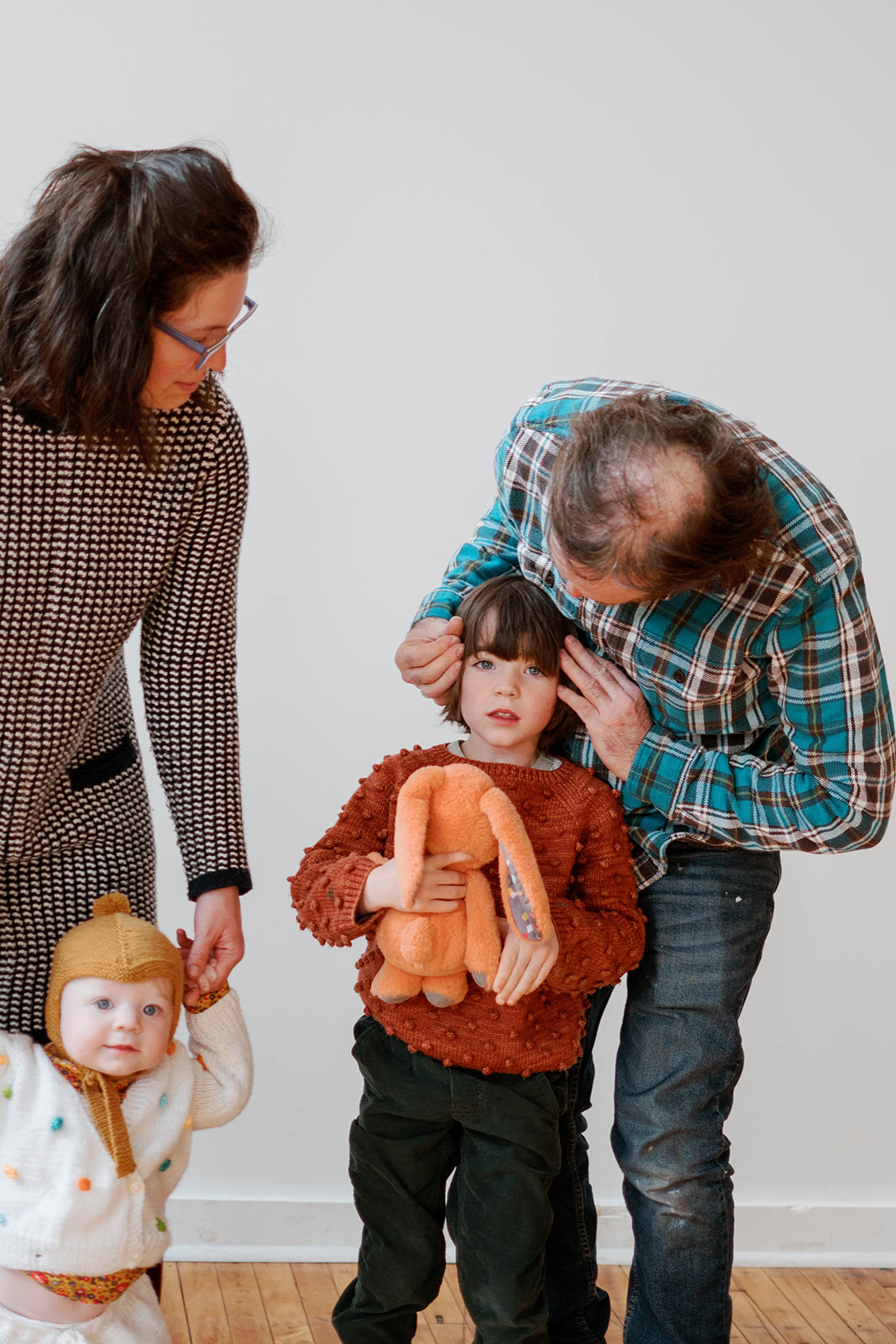 A dad fixes his child's hair while the child holds an orange stuffed bunny