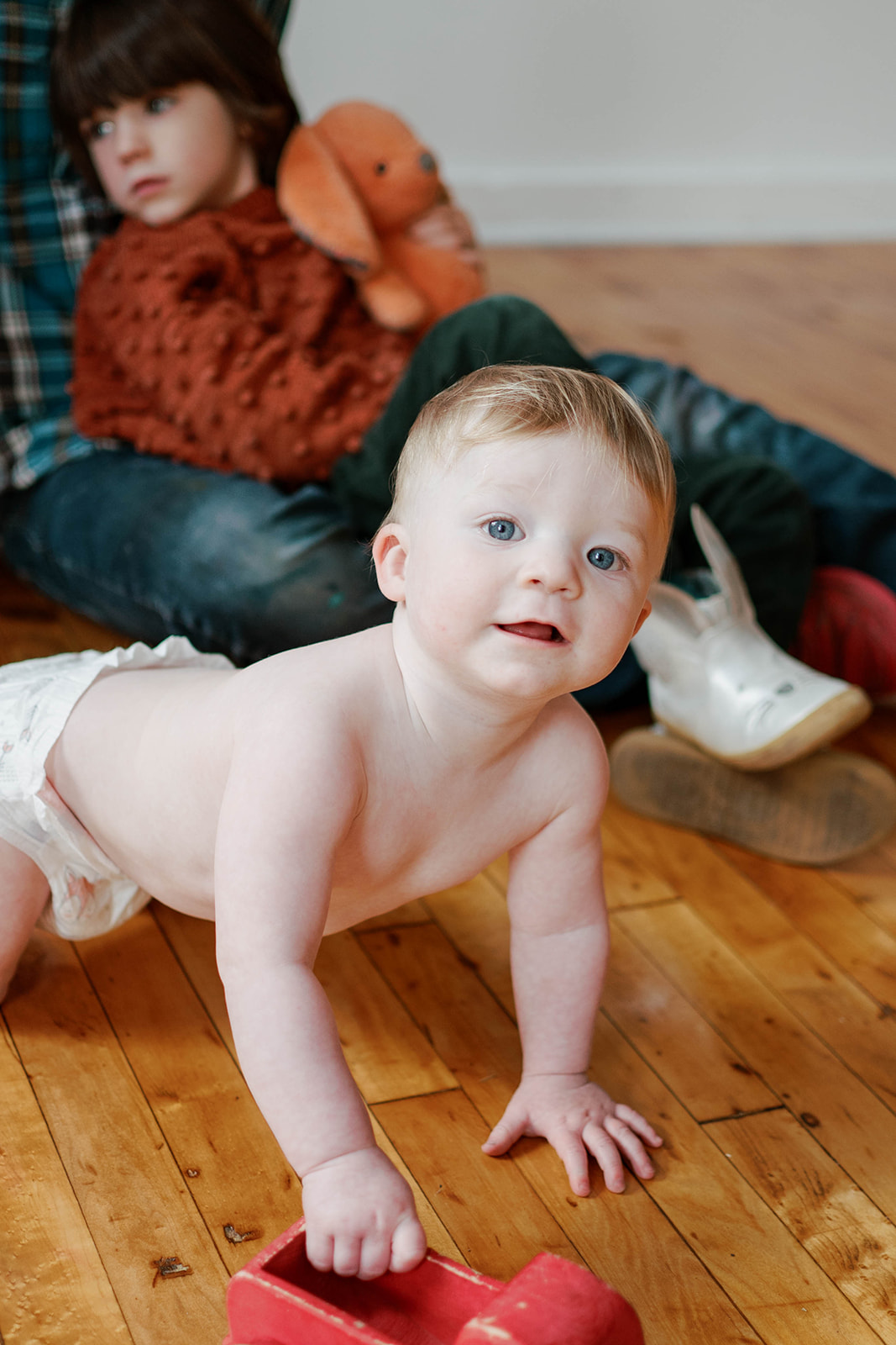 A baby in a diaper plays with a red truck