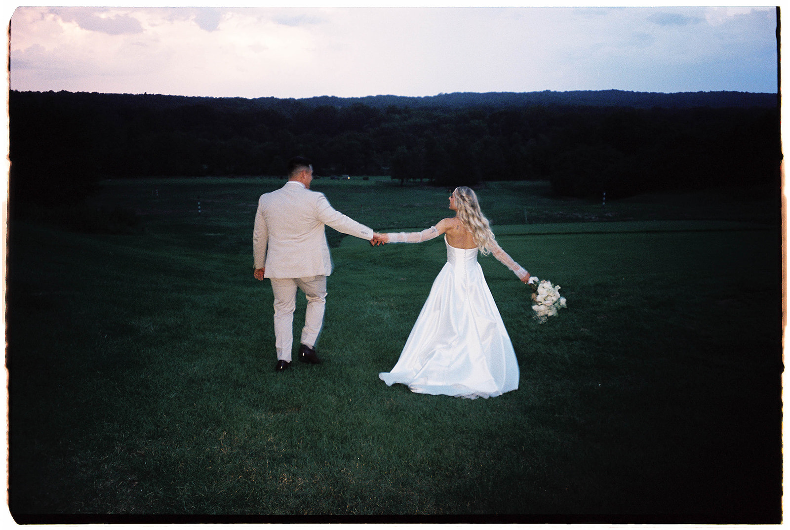 A wedding couple holding hands running together on a golf course at dusk