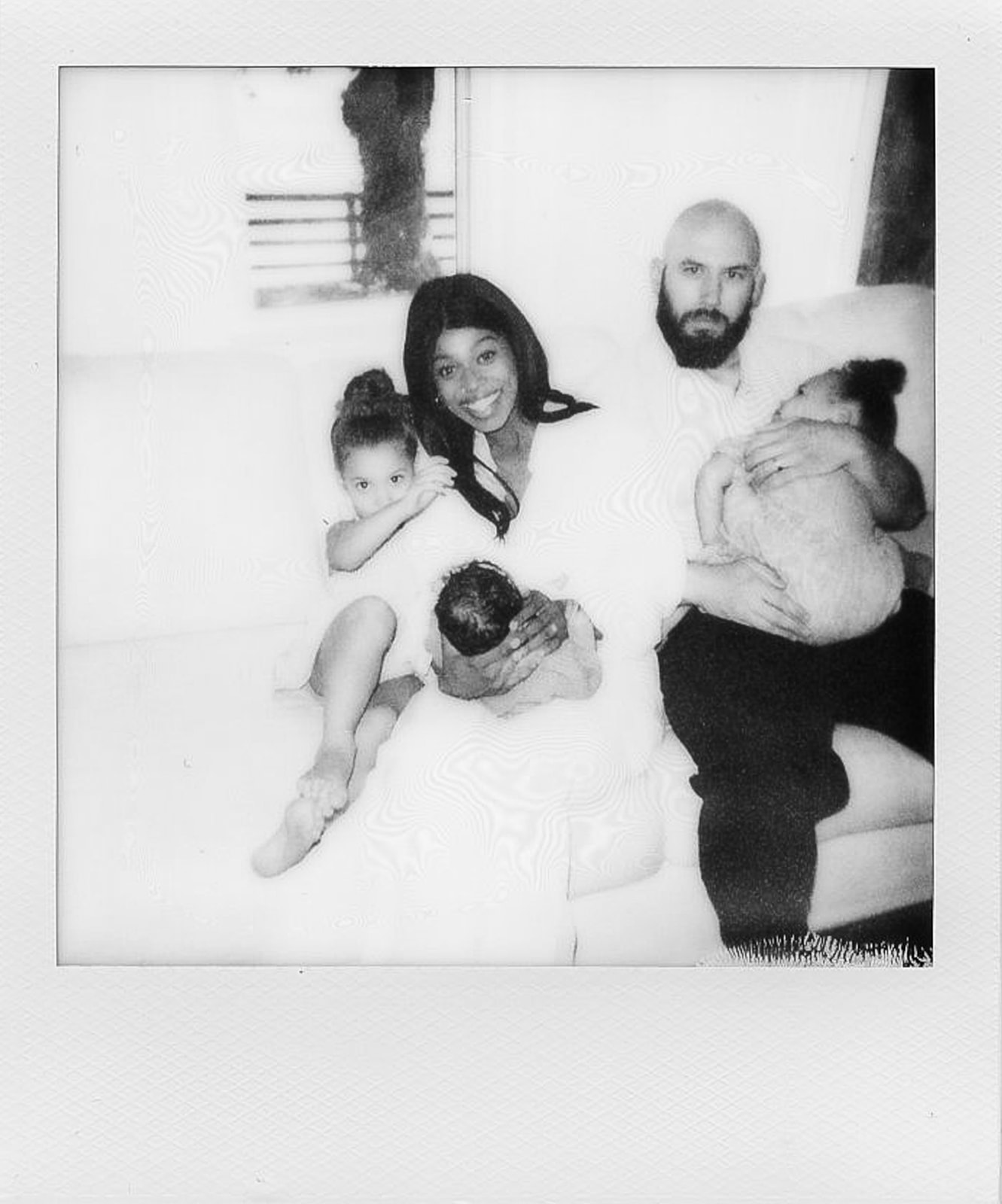 A black and white Polaroid of a family with three young girls sitting on a white couch 
