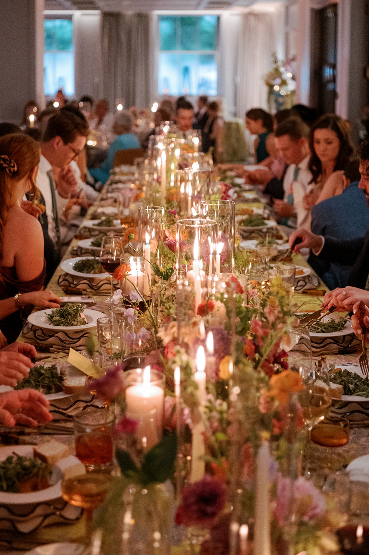 Guests sitting at a long, family-style table during dinner at a wedding reception