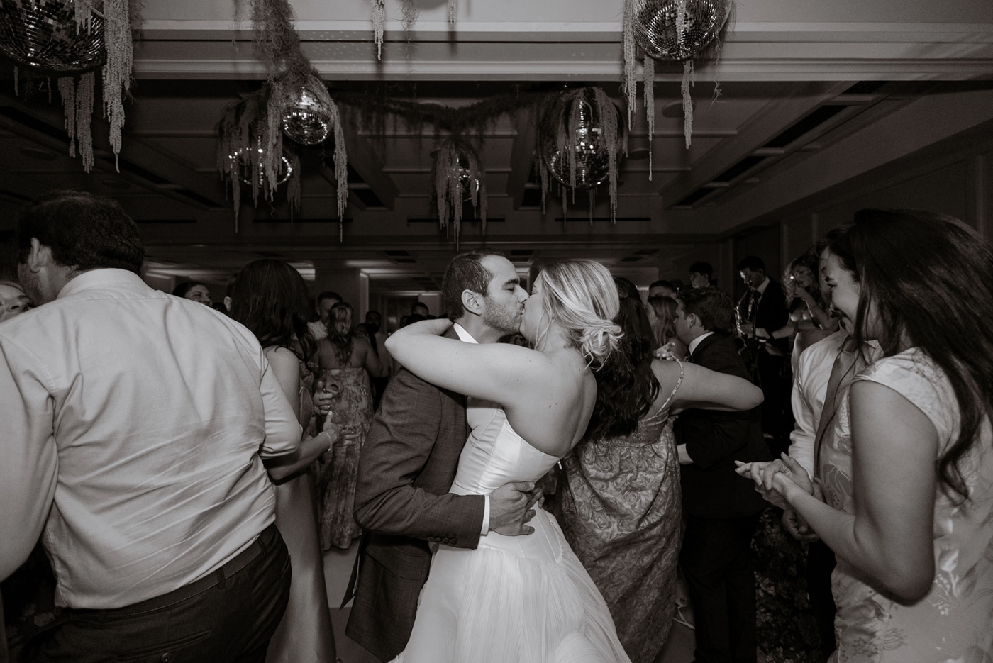 A bride and groom kiss on a crowded dance floor