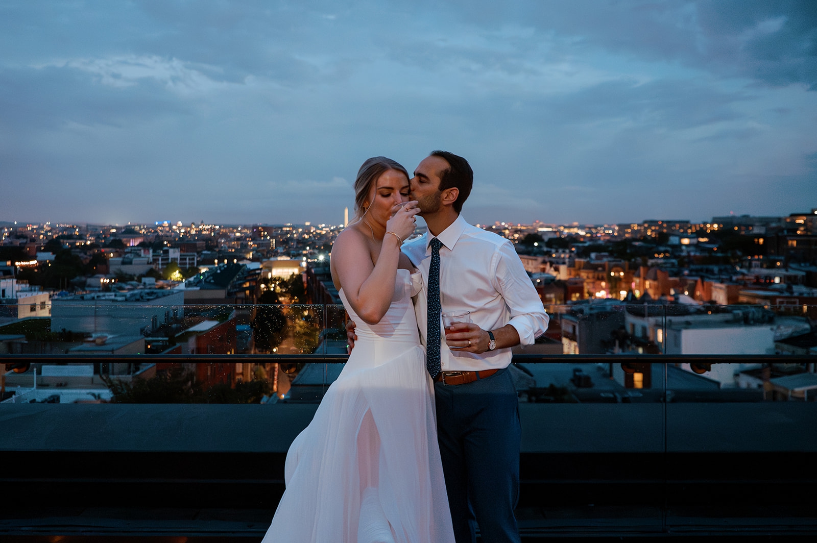 A bride and groom stand on the rooftop of the line hotel and toast