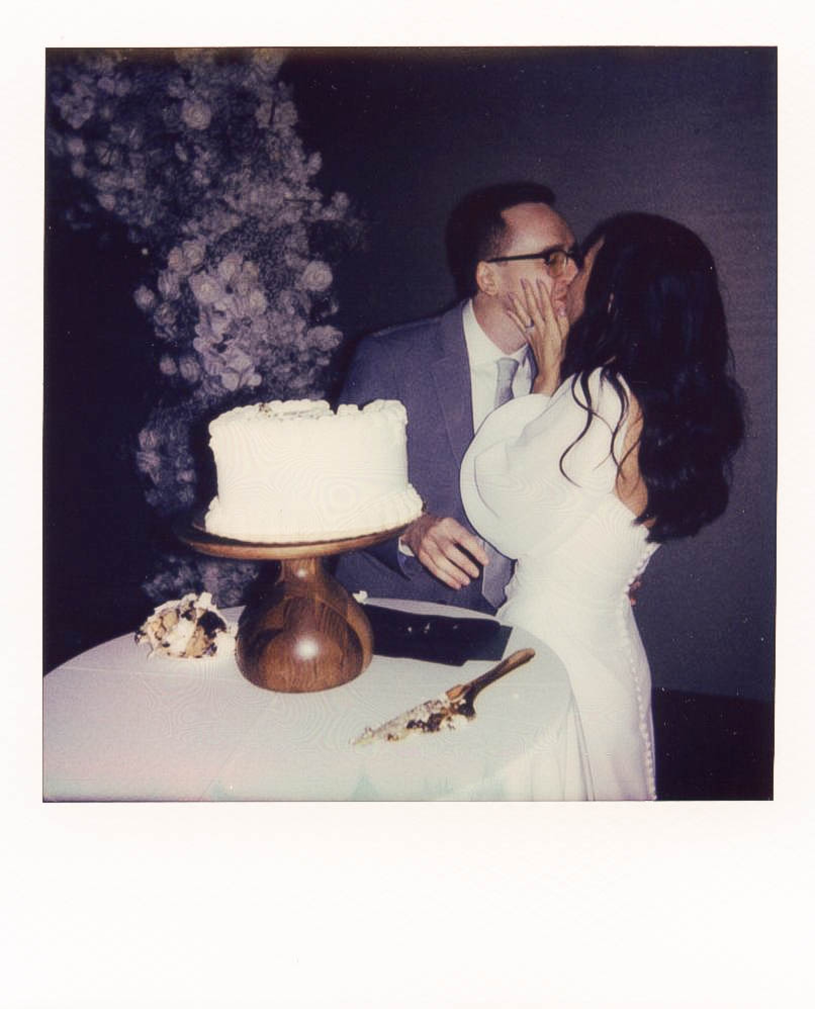 A polaroid photo of a bride and groom kissing as they cut their wedding cake 