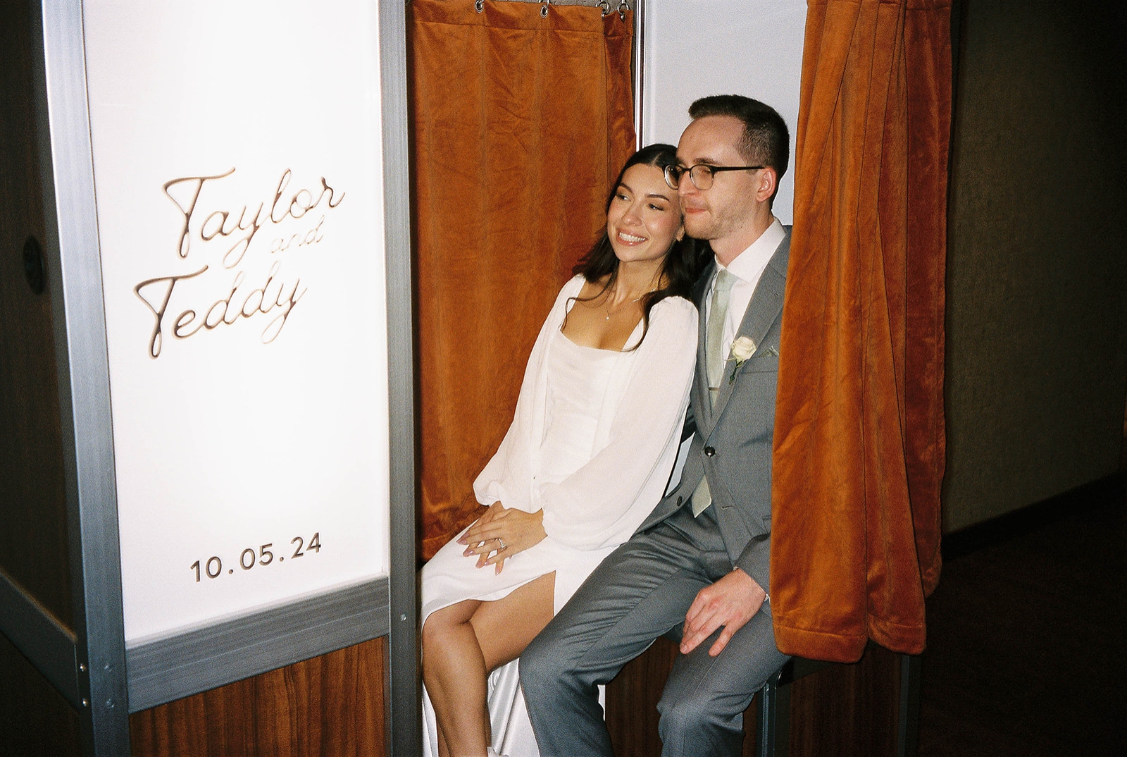 A bride and groom sit in a customized photo booth during their wedding reception