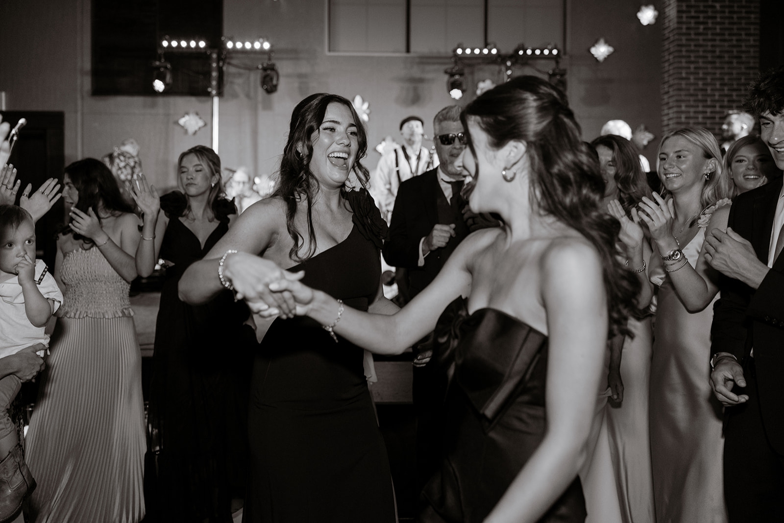 Two bridesmaids in black silk dresses dance during a wedding reception at the Archer Hotel Tysons