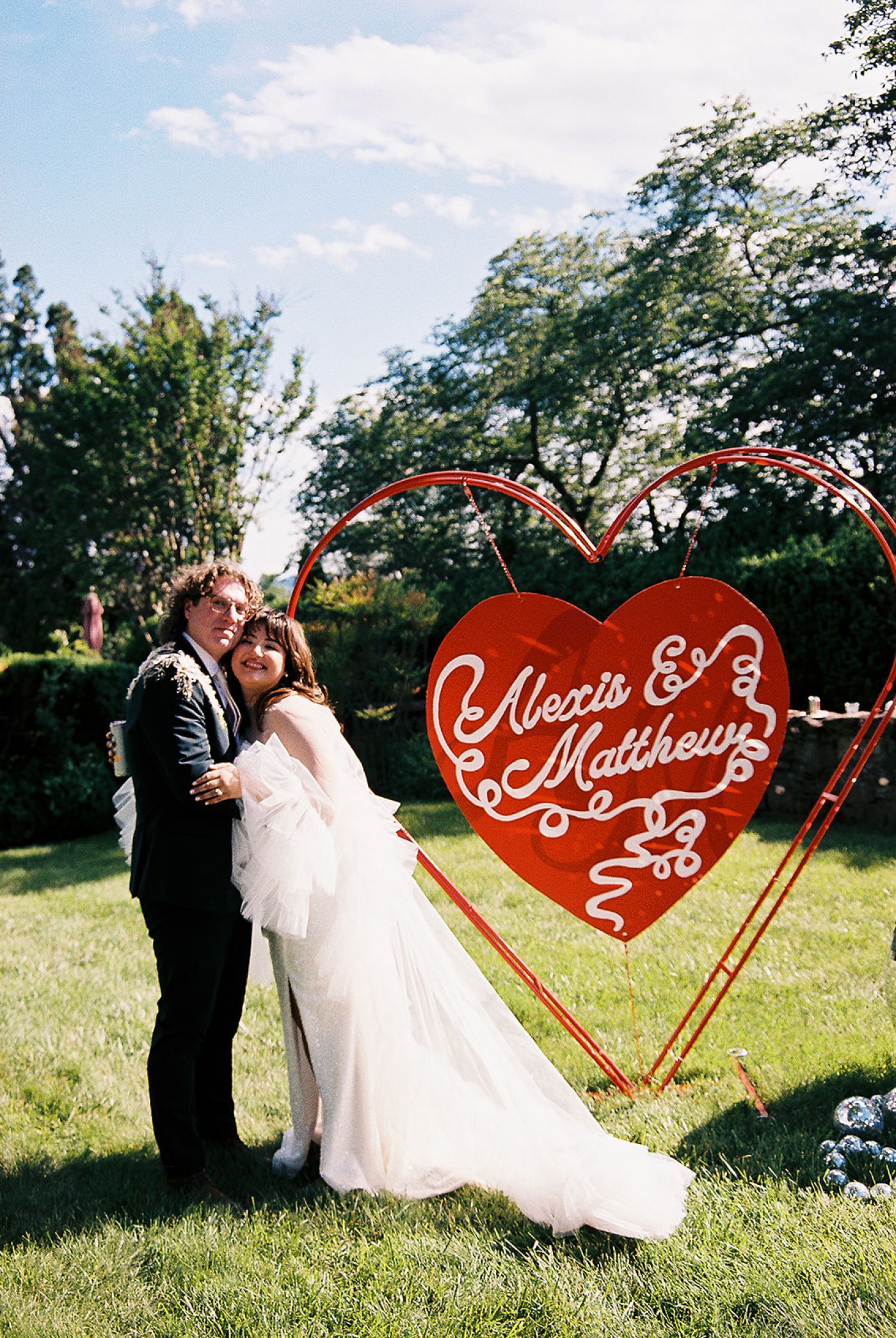 A bride and groom stand beside a heart-shaped welcome sign at Little Oatlands