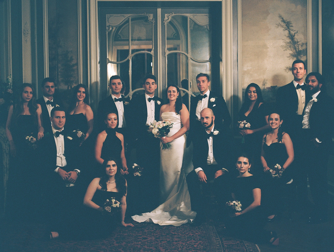 A bride and groom with a large wedding party in black silk dresses and tuxedos