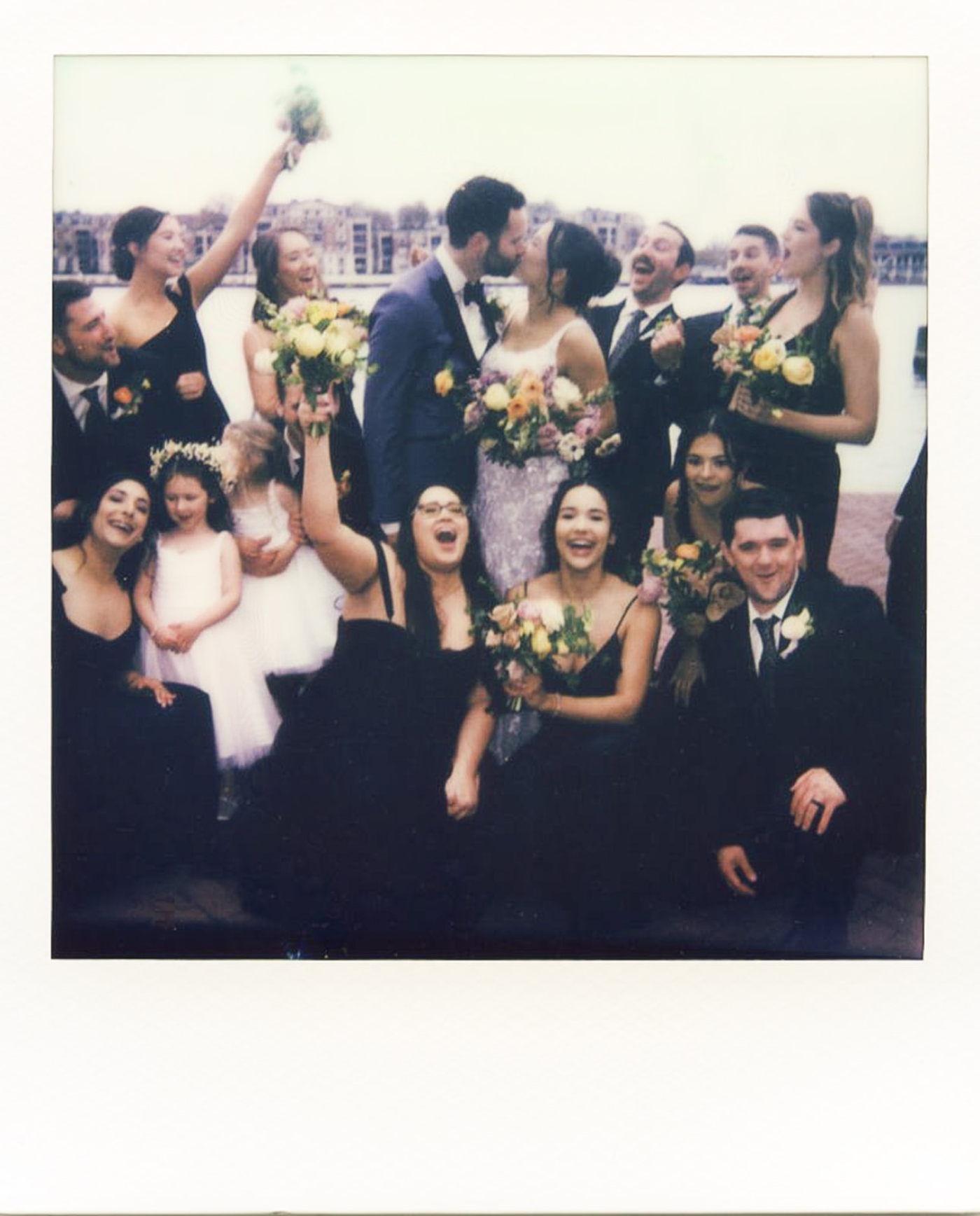 A polaroid scan of a bride and groom kissing while their wedding party cheers