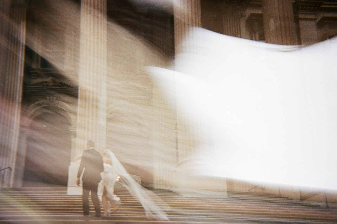 A film photo of a bride and groom walking up the stairs of New York City Hall