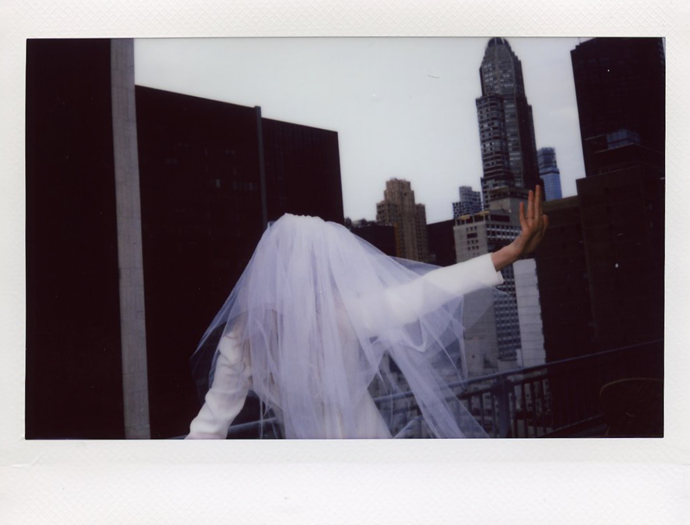A polaroid of a bride in an elbow-length veil looking over the city from a balcony at the Plaza Hotel