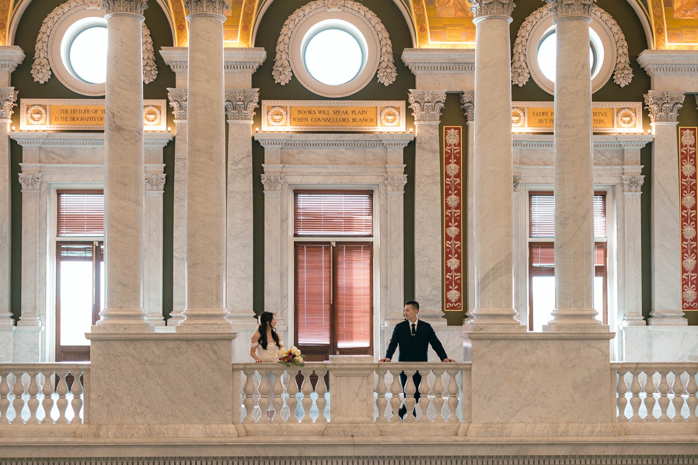 A bride and groom lean over a balcony inside the Library of Congress 