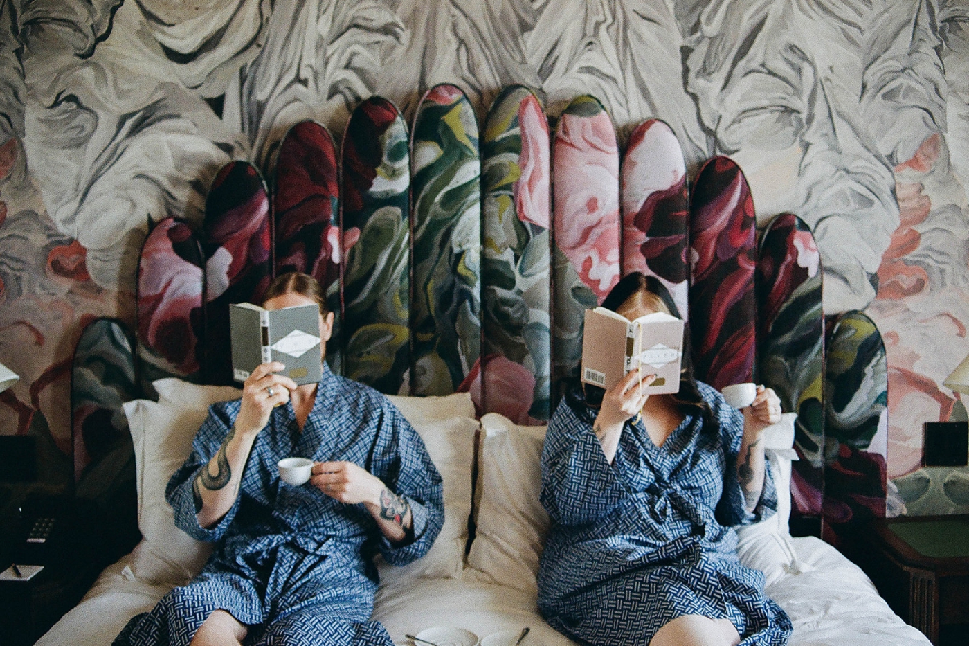 A bride and groom in blue robes holding books over their faces 