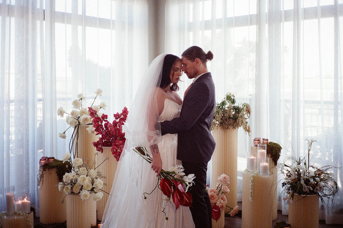A bride and groom in the Riggs Hotel ballroom surrounded by short pillars topped with bold florals 