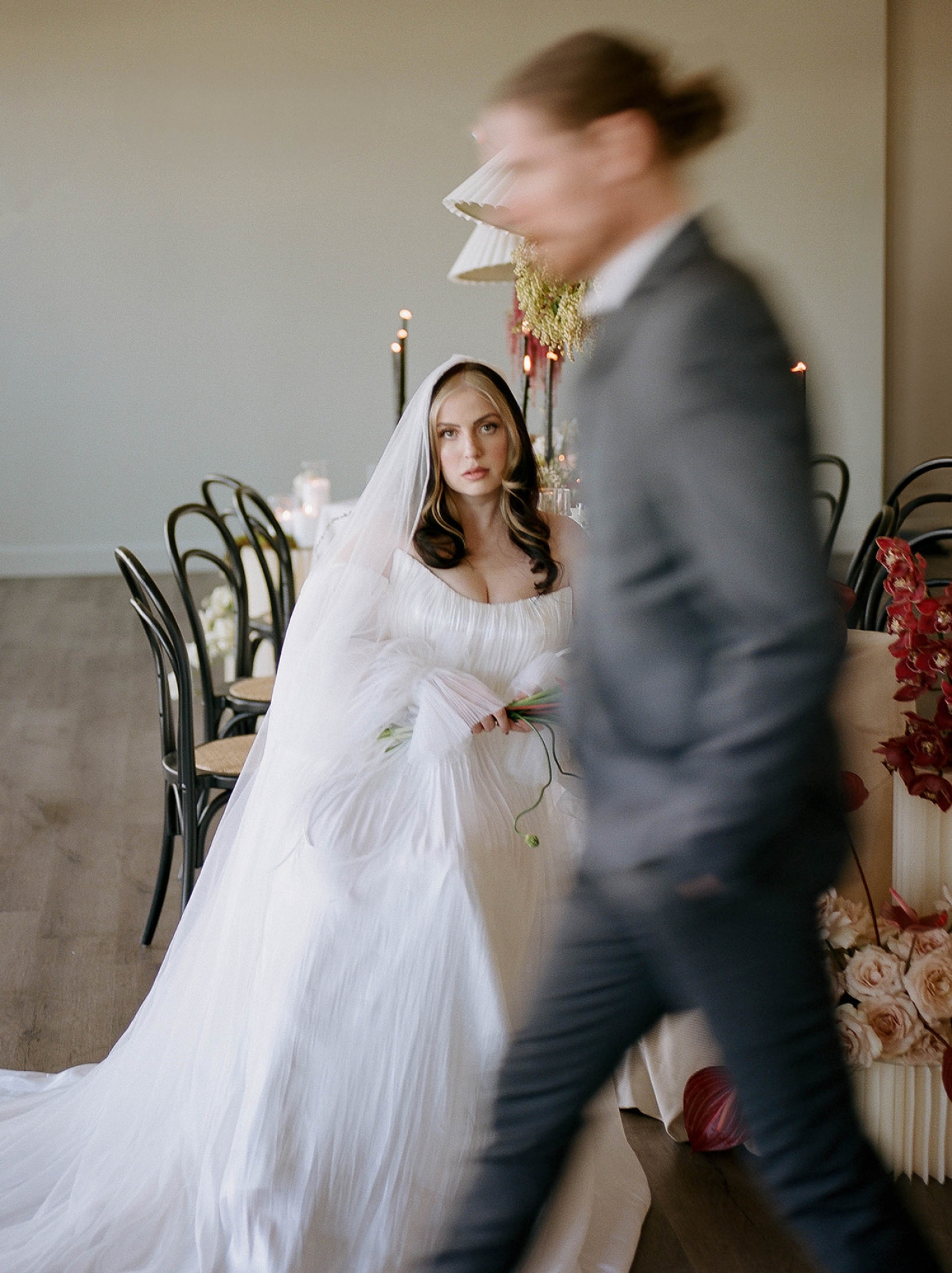 A groom walks in front of the bride, who is seated at a wedding reception table in the Riggs Hotel ballroom 