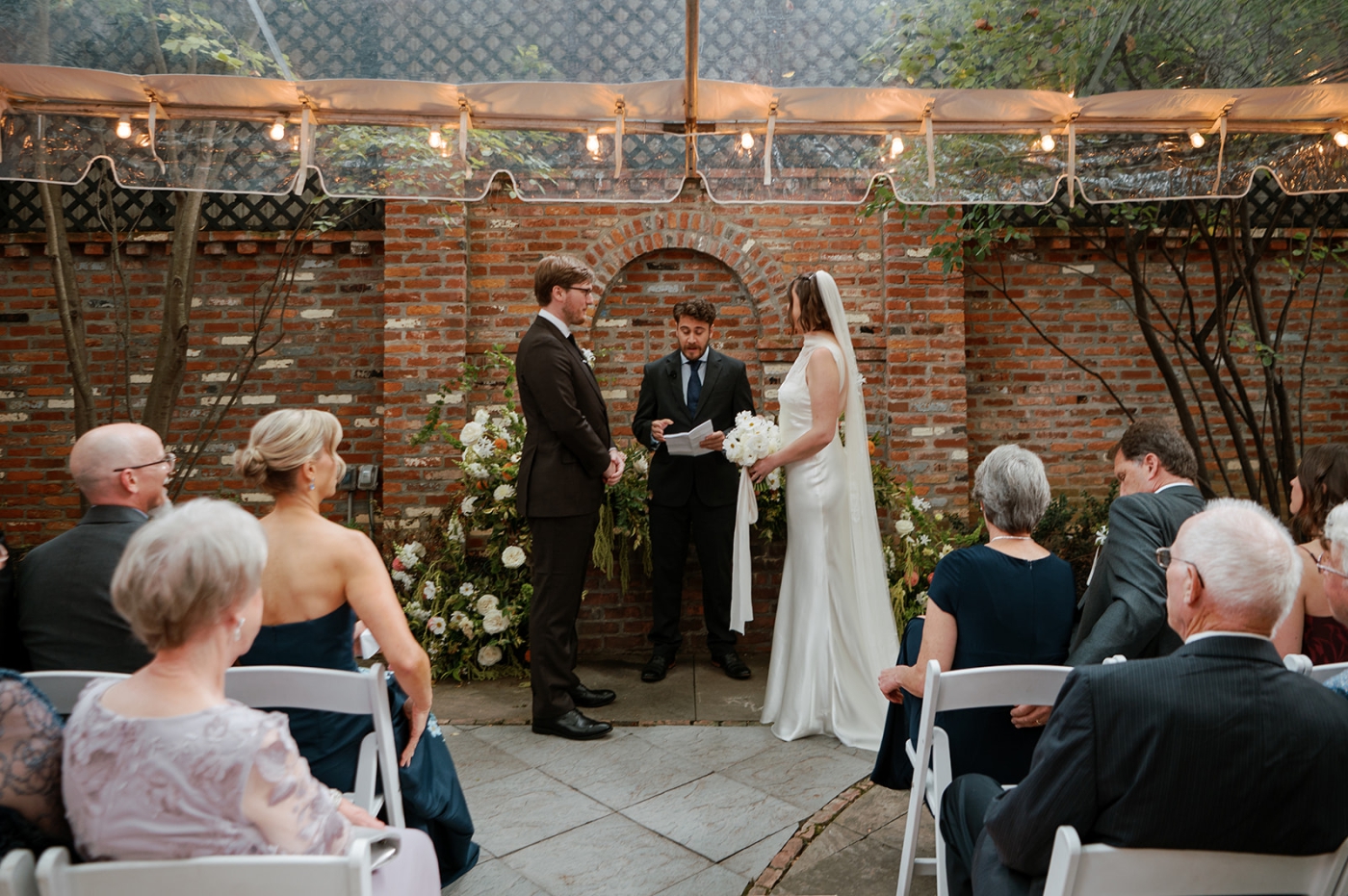 A bride and groom standing at the altar beneath a clear top tent in the courtyard of the Fathom Gallery 