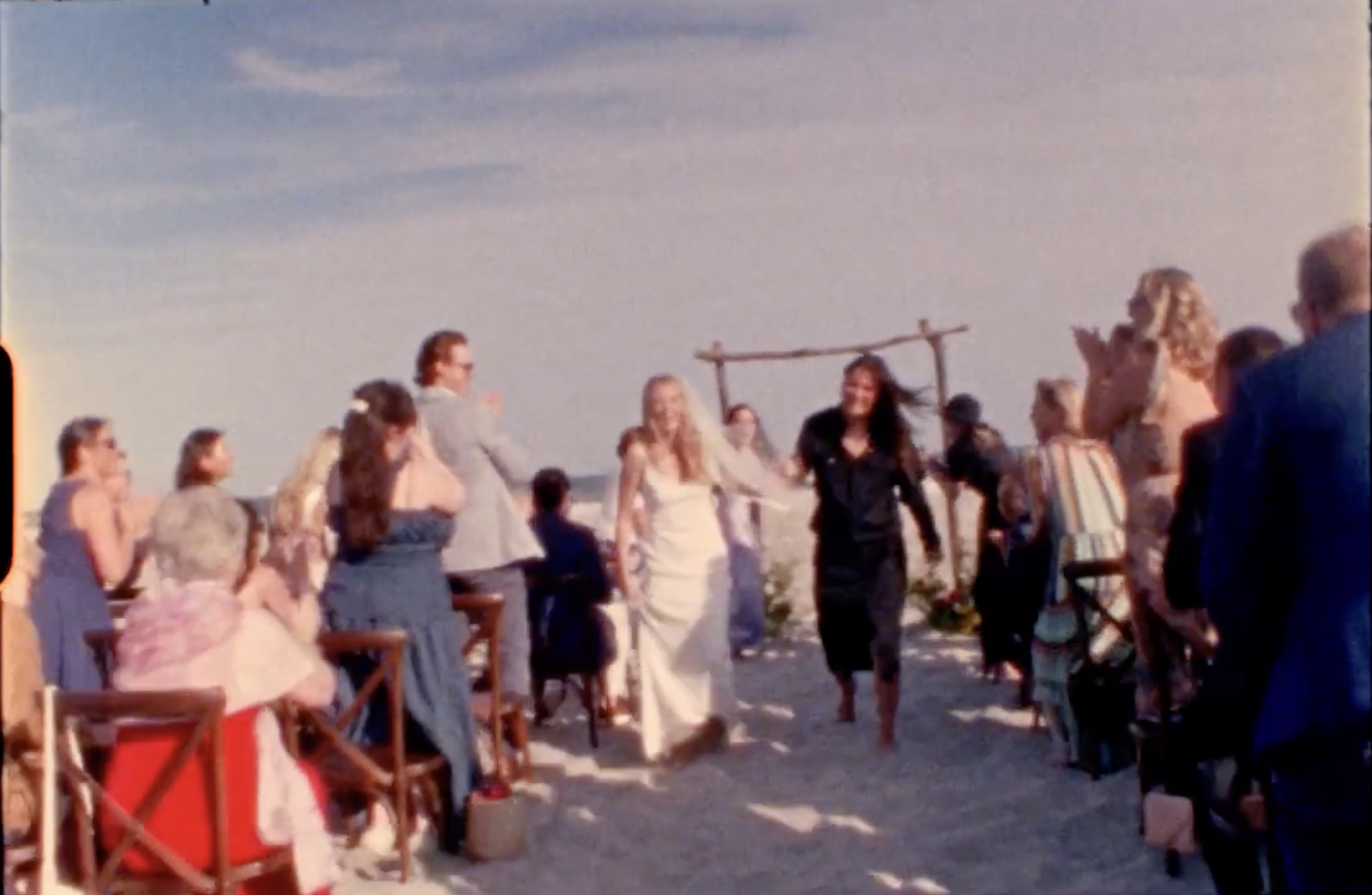 A screenshot from a Super 8 video of two brides walking back up the aisle at their beach wedding