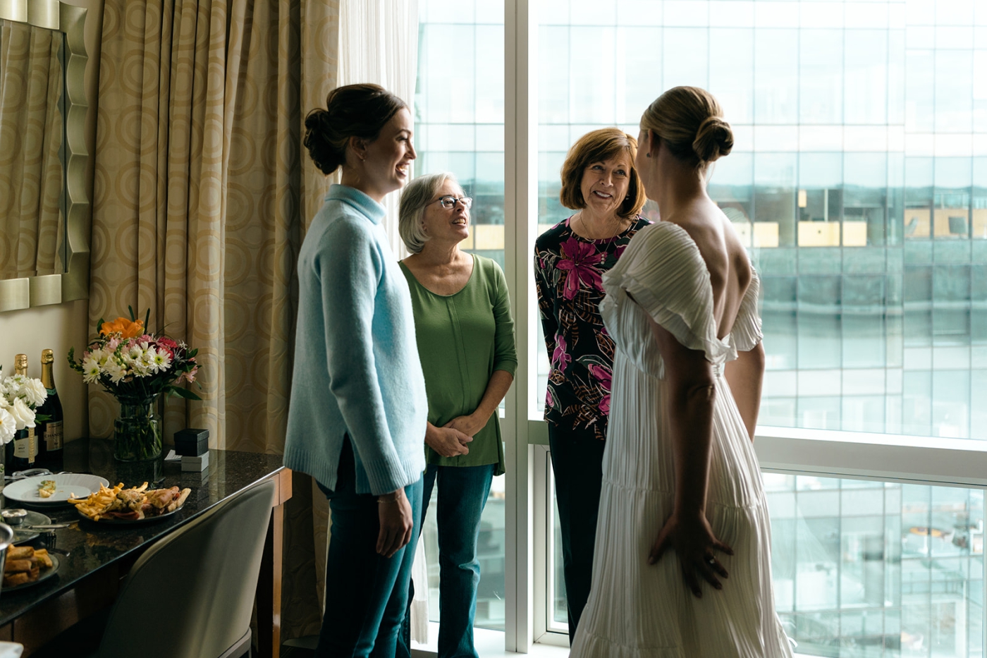 A bride stands in front of a window and talks with her mother and grandmother in the Four Seasons Hotel in Baltimore